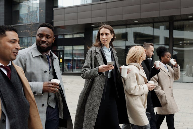 Directors 4 A diverse group of business professionals walking outside a modern building, enjoying coffee and conversation.
