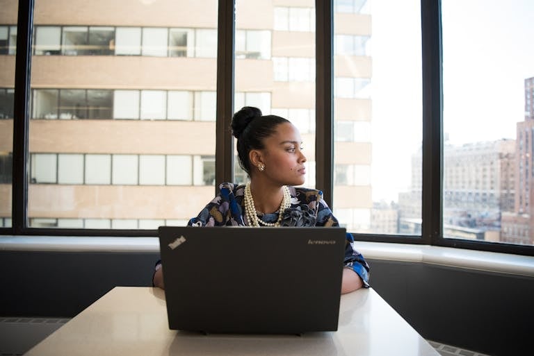 Directors 2 Confident woman working on a laptop in an office with large windows and city view.