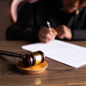 Judge signing documents at desk with focus on gavel, representing law and justice.